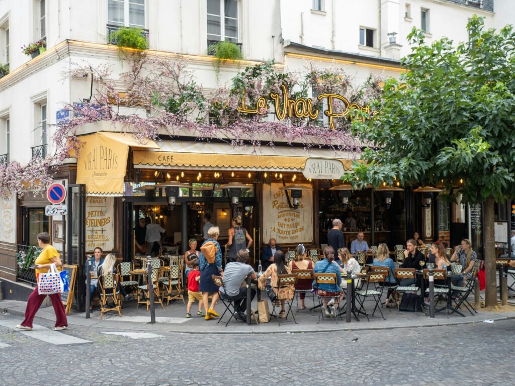 Colombia sube los salarios 23%: lo que esto significa para Bitcoin, el dólar y tu dinero Outdoor view of Le Vrai Paris bistro in Montmartre, Paris, with people dining and vibrant atmosphere.