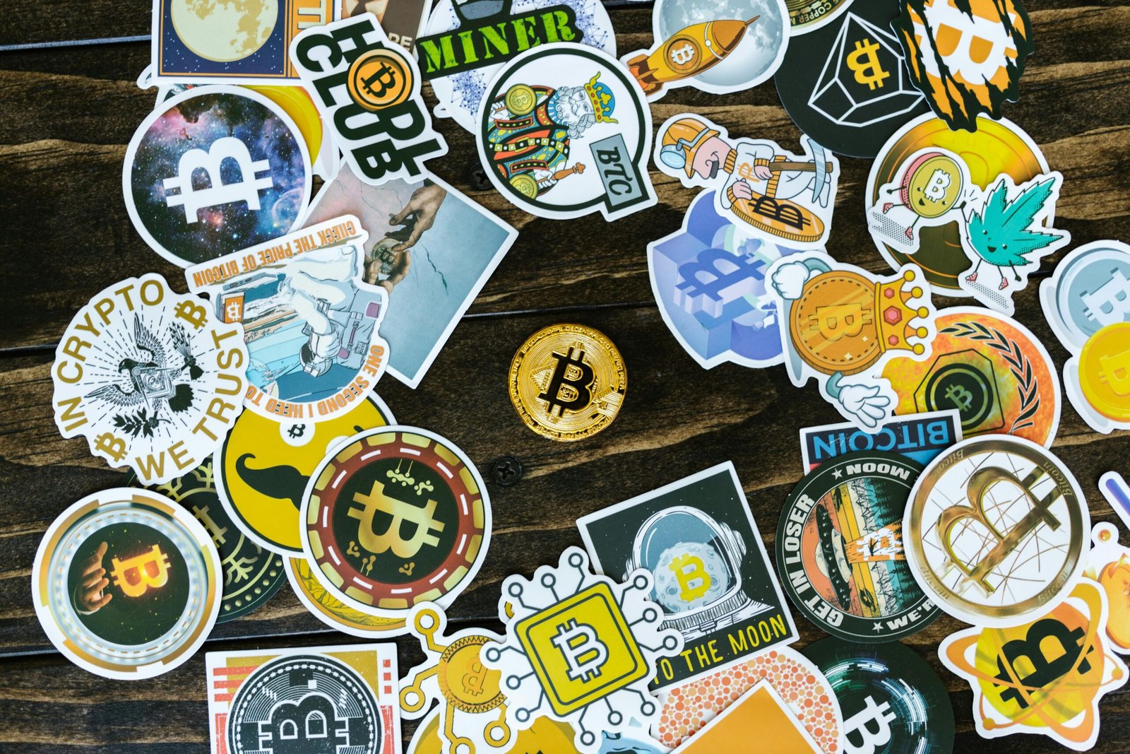 A collection of vibrant Bitcoin-themed stickers and a coin on a wooden surface. Ideal for cryptocurrency concepts.