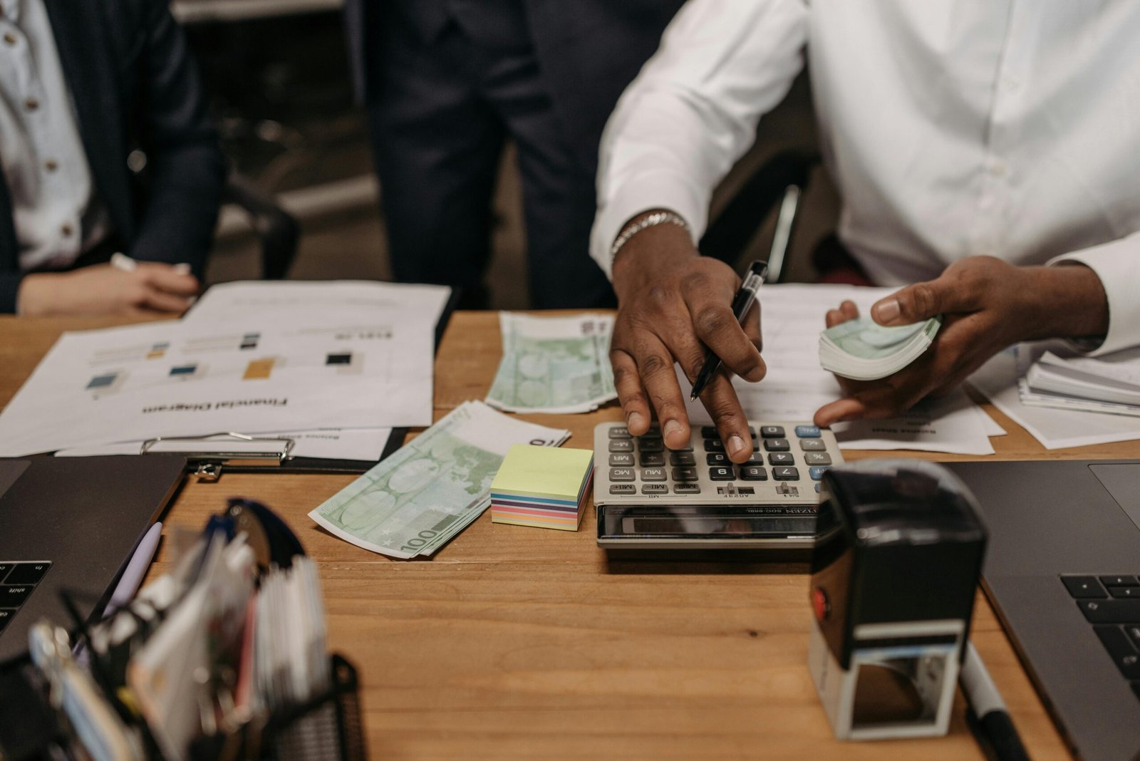 Professional setting with people handling cash and calculations using a calculator at a desk.